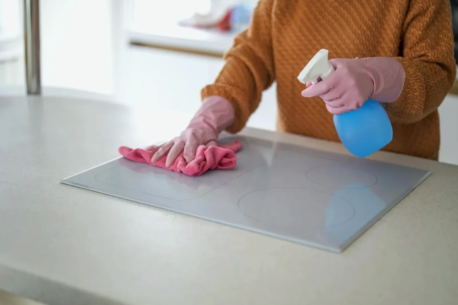 A gloved hand spraying and wiping a white countertop