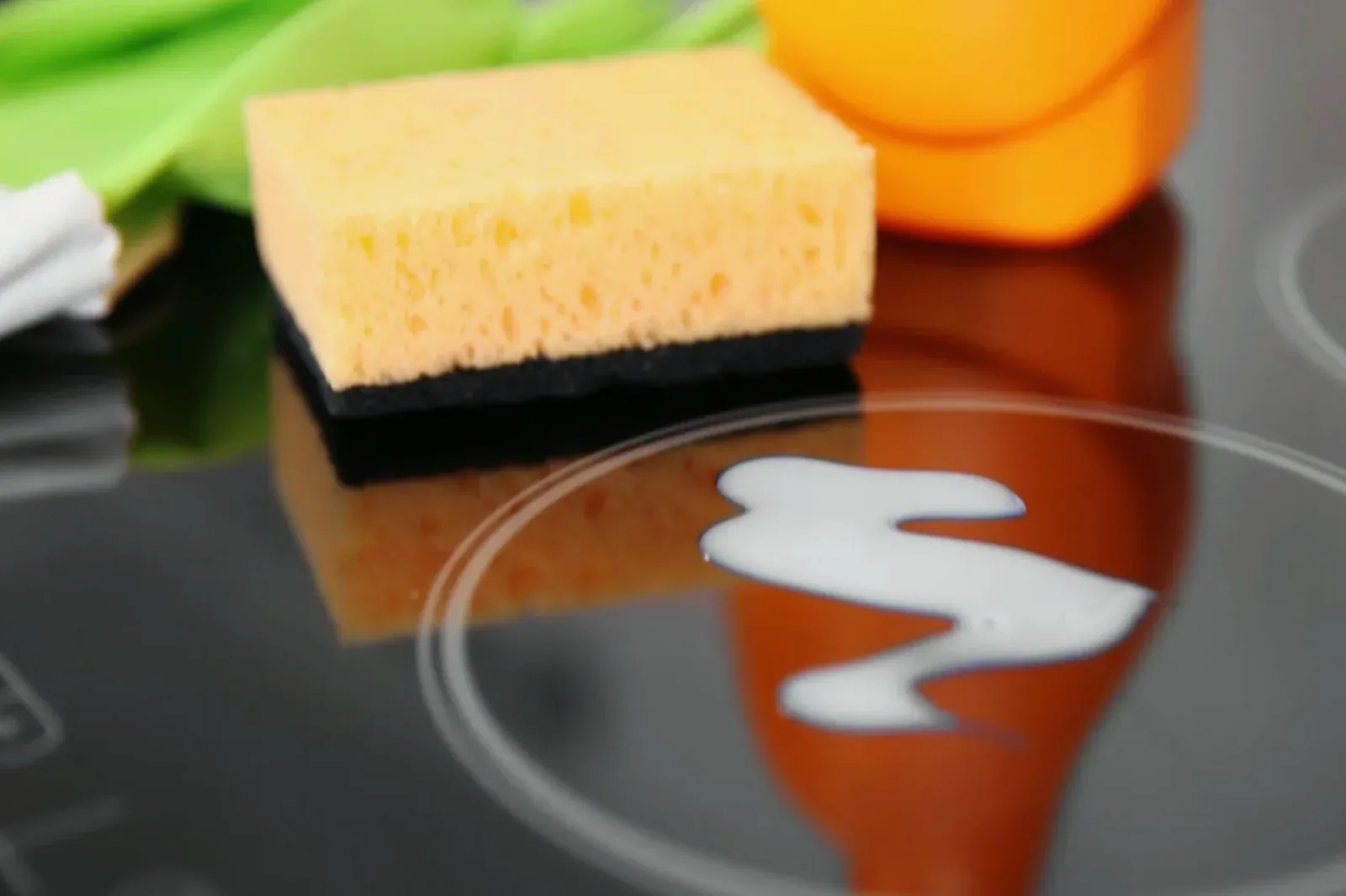 A sponge and cleaning spray on a glass cooktop